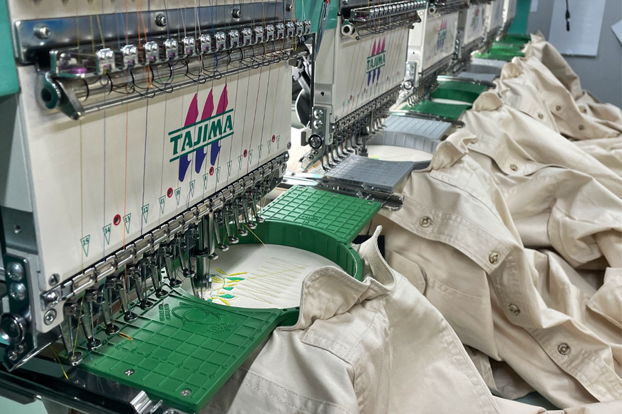 Multi-head embroidery machine stitching left-chest logos on a run of stone-coloured work shirts